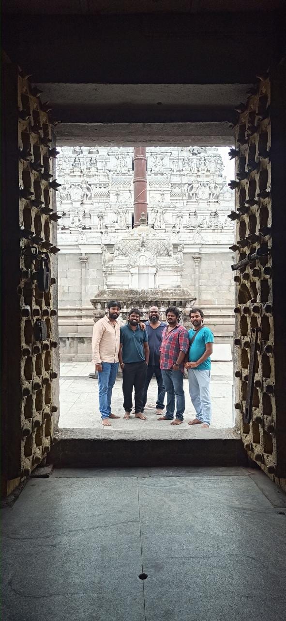 The team framed in a carved temple doorway, gopuram beyond